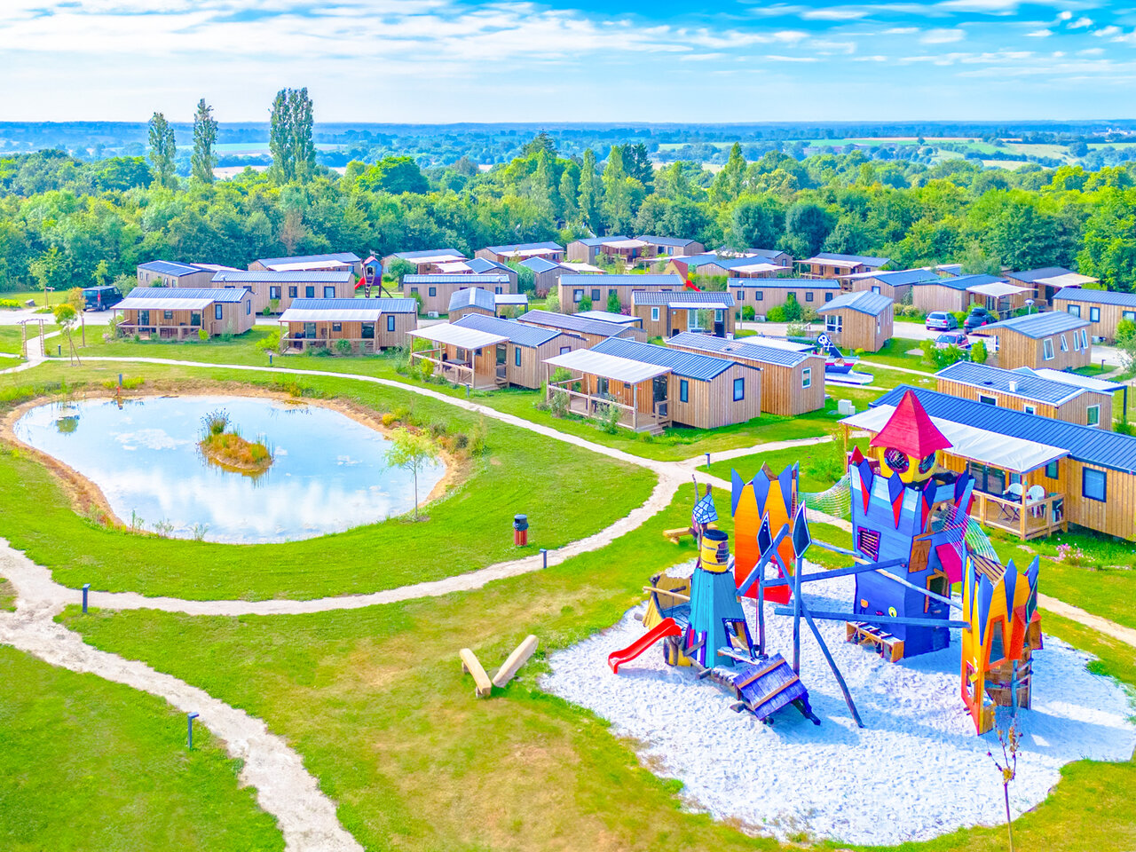 Zona de juegos colorida, estanque y mobil-homes en el camping CAPFUN Lac de Ribou en Cholet (49).