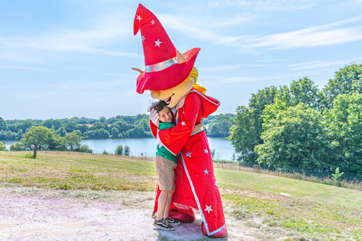 Niño sonriente abrazando la mascota del camping durante una animación en el camping CAPFUN Lac de Ribou en Cholet (49).