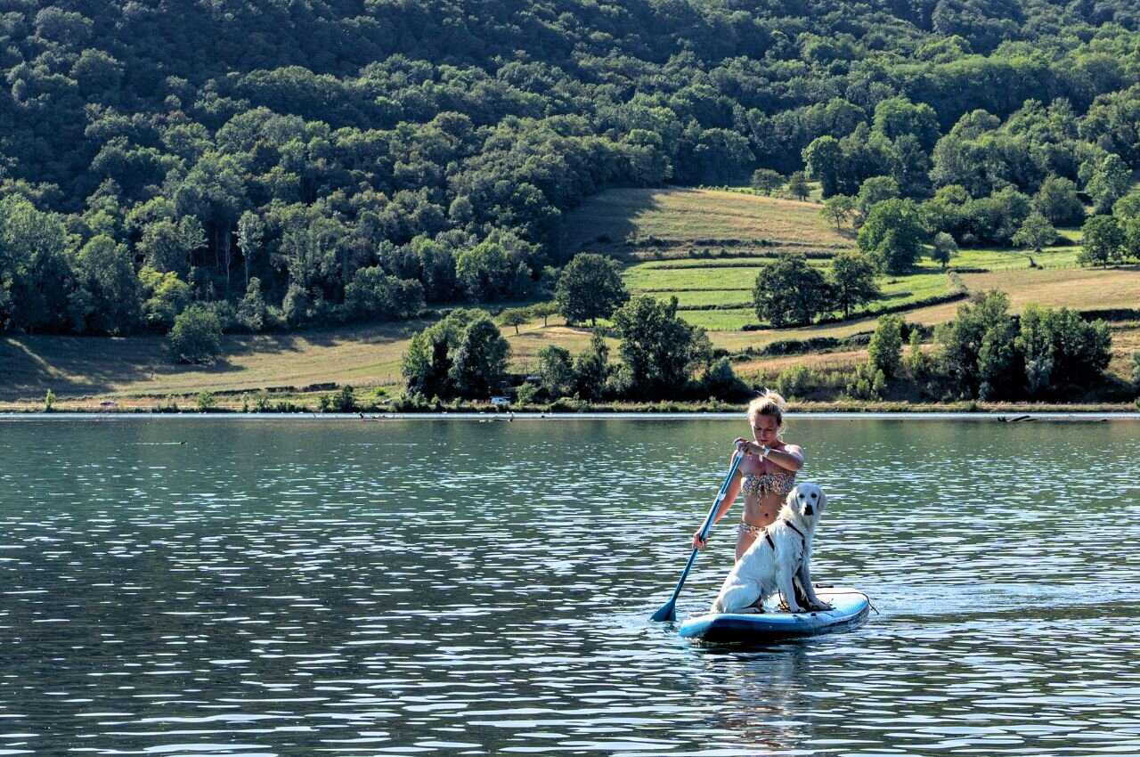 Mujer y perro en paddleboard, lago. En el camping CLICOCHIC Lac du Lit du Roi.