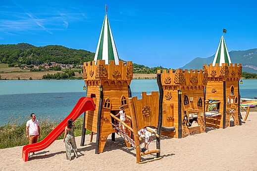 Parque infantil castillo de madera con tobogán rojo en el camping CLICOCHIC Lac du Lit du Roi en Massignieu-de-Rives (01).