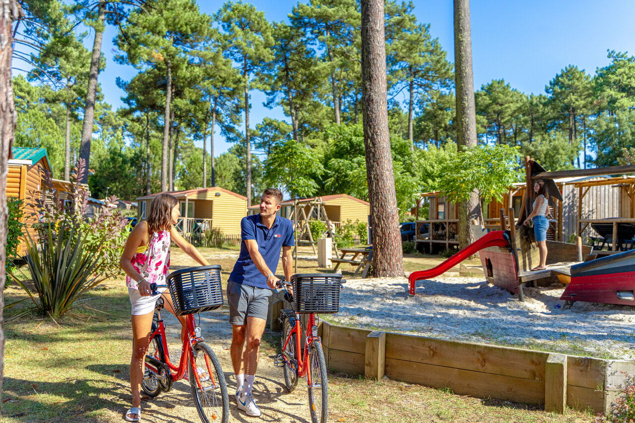 Pareja con bicicletas y parque infantil en el camping CAPFUN Landisland en Moliets-et-Maa.