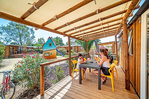 Familia comiendo en la terraza de un Mobil-home con zona de juegos en el camping CAPFUN Las Bousigues en Le Barcarès (66).