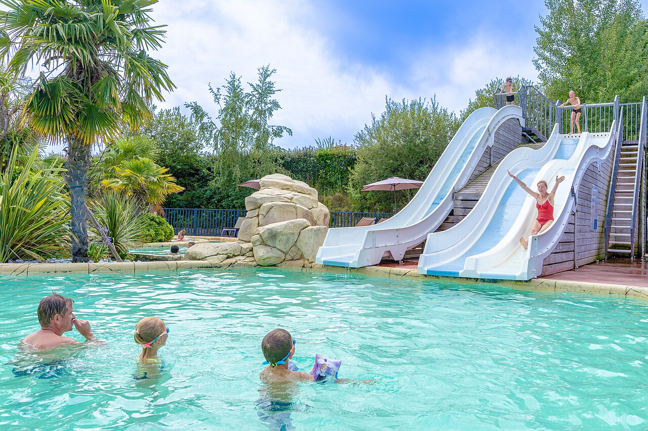 Piscina exterior con toboganes y familia en el camping VAGUES OCEANES Les Iles en Hudimesnil (50).