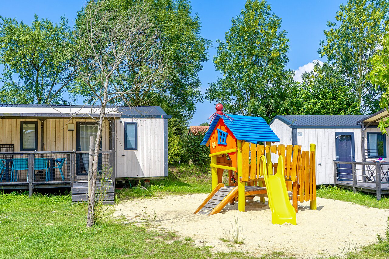 Parque infantil colorido y mobil-homes modernos en el camping VAGUES OCEANES Les Iles en Hudimesnil (50).