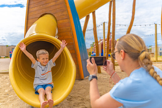 Niño sonriente en un tobogán amarillo en el parque infantil del camping VAGUES OCEANES Licorne en Dunkerque (59).