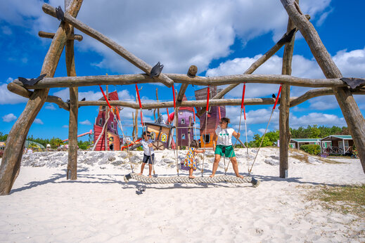 Zona de juegos con puente de cuerda y estructuras coloridas en el camping CAPFUN Lila en LINXE (40).