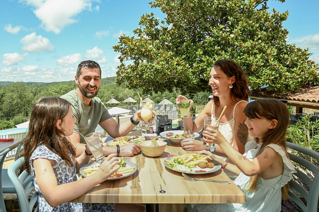 Familia feliz almorzando en la terraza del restaurante-bar en el camping CLICOCHIC Linotte en Le Bugue.