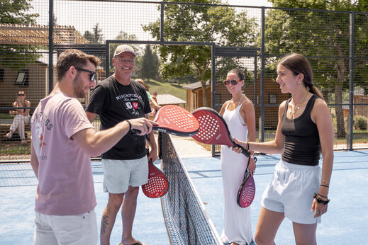 Familia sonriente jugando al pádel en la cancha multideporte del camping CLICOCHIC Linotte en Le Bugue (24).