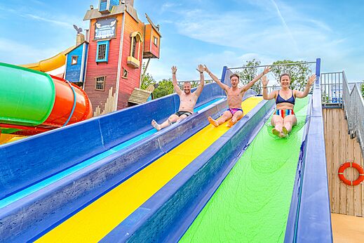 Tres personas deslizándose por toboganes acuáticos coloridos en el camping CAPFUN Lodge en SARZEAU (56).