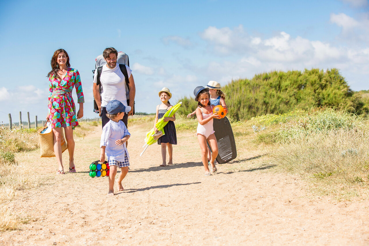 Familia caminando por sendero de arena con equipo de playa en el camping CAPFUN Loubine en Les Sables d'Olonne (85).