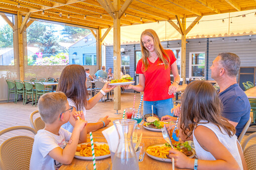 Camarera CAPFUN sirviendo comidas a una familia en el restaurante del camping CAPFUN Loubine en Les Sables d'Olonne (85).
