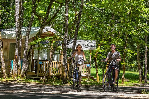 Pareja en bicicleta en sendero arbolado en camping CLICOCHIC Lou Castel, Castelnaud-la-Chapelle.