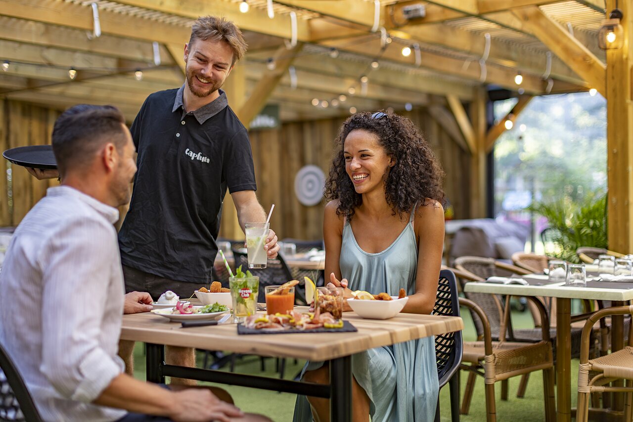 Pareja cenando en terraza, camarero sonriente en CAPFUN Lou Puntaou en LEON.