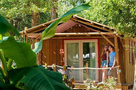 Mobil-home de madera con terraza y pareja sonriente en el camping CAPFUN Lou Puntaou en LEON (40).