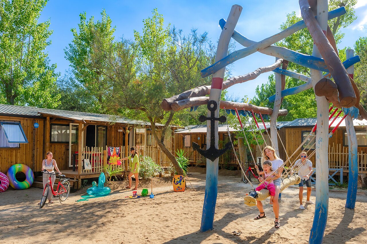 Zona de juegos con columpio y Mobil-homes en el camping CAPFUN Lou Village en Vendres (34).