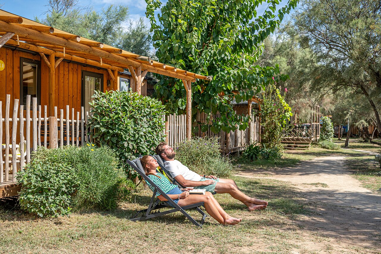 Pareja relaj�ndose en tumbonas frente a Mobil-home de madera en camping CAPFUN Lou Village.