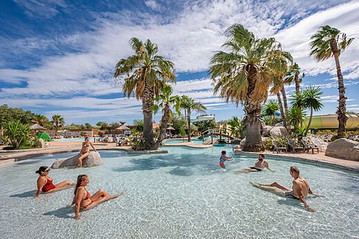 Piscina exterior, tobogán y palmeras en el camping CAPFUN Lou Village en Vendres (34).