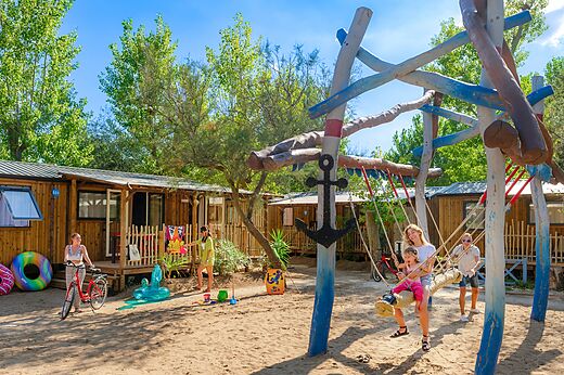 Zona de juegos de madera, columpio, familia y Mobil-homes en camping CAPFUN Lou Village.