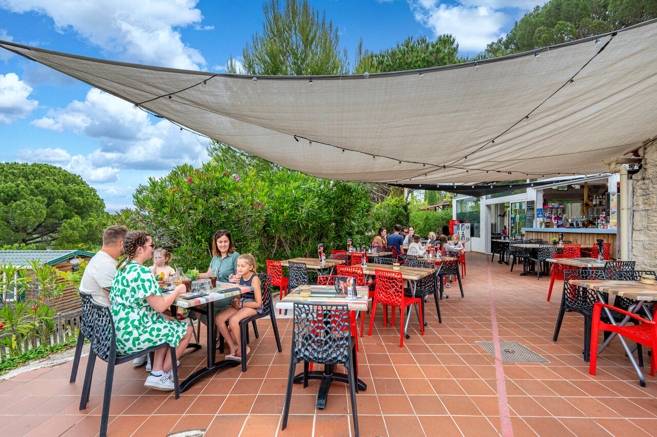 Terraza de restaurante sombreada con familias y bar en el camping CAPFUN Malissonne en LA CADIERE D'AZUR (83)