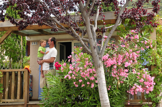 Casa móvil con terraza florida y familia sonriente en el camping CAPFUN Malissonne en LA CADIERE D'AZUR (83).