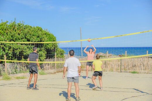 Campo de voleibol de arena con jugadores y mar al fondo en el camping CAPFUN Marina d'Al�ria en Aleria (20).