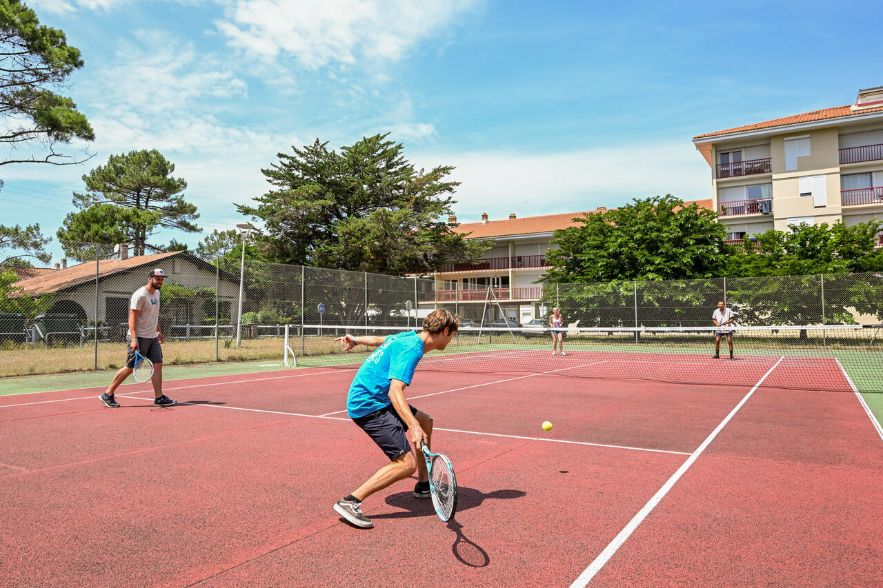 Pista de tenis exterior con jugadores activos en el camping VAGUES OCEANES Marina Landes en Mimizan (40).