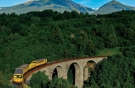 Tren amarillo cruzando viaducto de piedra en los Pirineos, lugar para visitar.