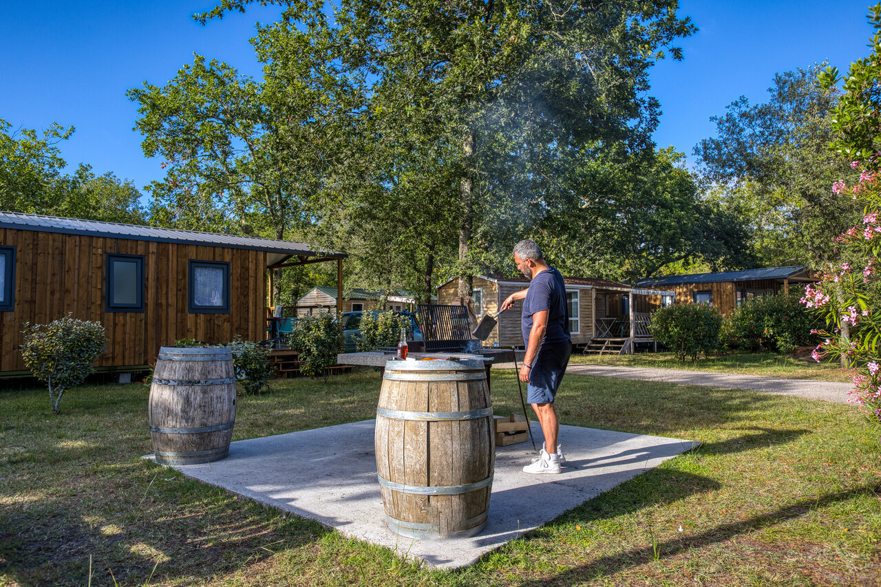 Hombre haciendo barbacoa frente a Mobil-homes en camping CLICOCHIC M�doc Bleu Carcans (33).