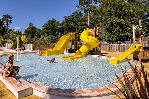 Piscina con toboganes acuáticos amarillos en el camping CLICOCHIC Médoc Bleu en Carcans (33).