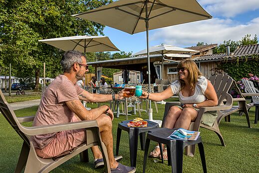 Pareja brindando con cócteles en el bar del camping CLICOCHIC Médoc Bleu en Carcans (33).