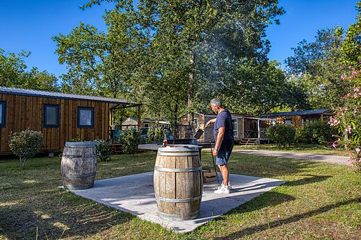 Hombre haciendo barbacoa frente a Mobil-homes en camping CLICOCHIC Médoc Bleu Carcans (33).