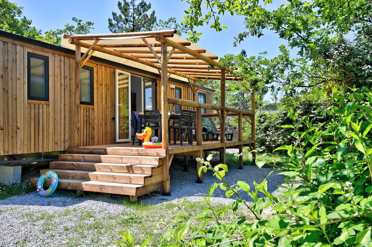 Mobil-home de madera con terraza sombreada, mobiliario exterior y naturaleza en el camping CAPFUN Merle Roux en Baix (07).