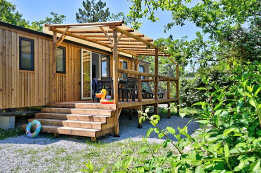 Mobil-home de madera con terraza cubierta y mobiliario exterior en el camping CAPFUN Merle Roux en Baix (07).