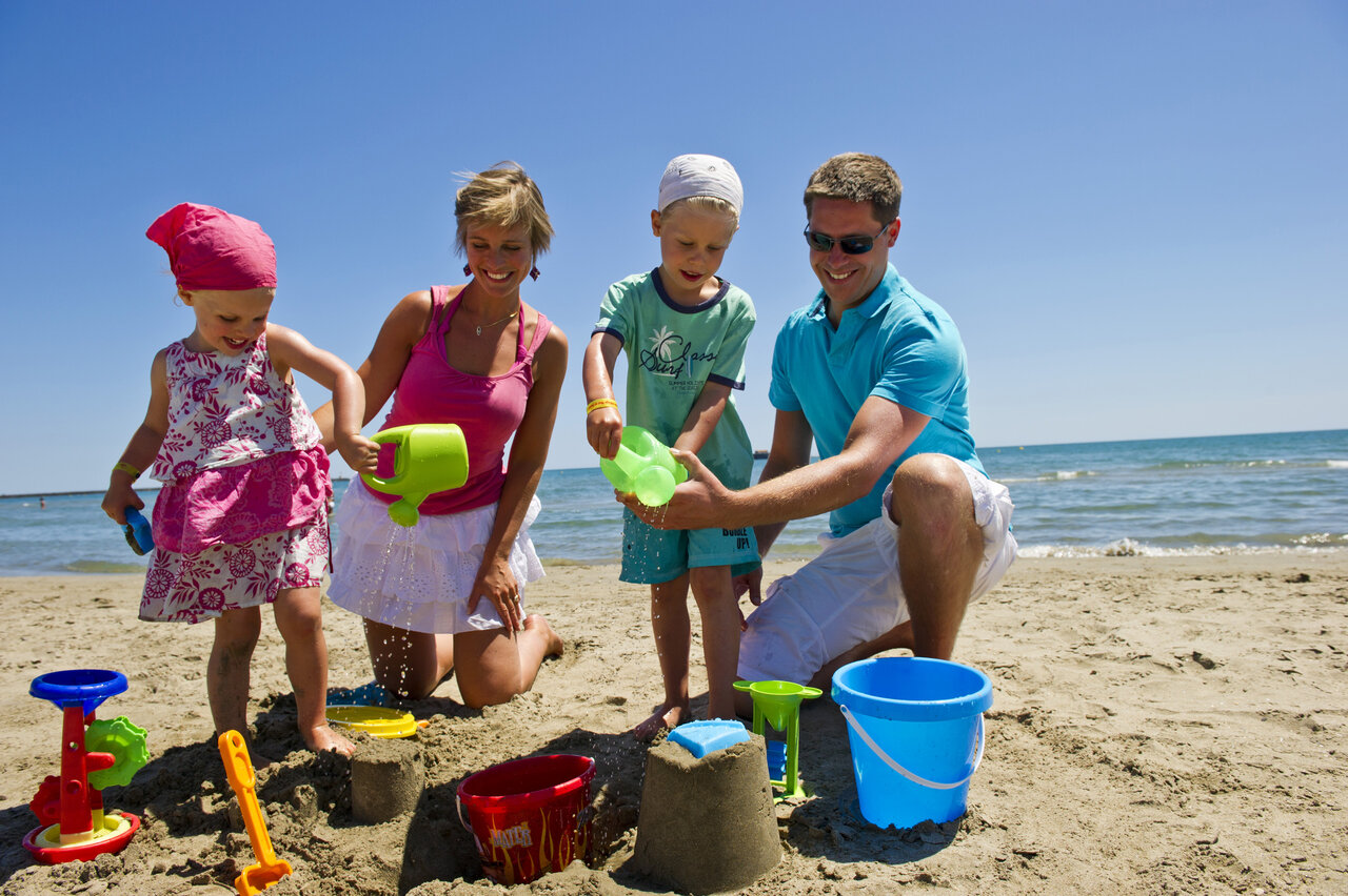Familia construyendo castillos de arena en la playa del camping CAPFUN Mer et Soleil en Cap d'Agde.