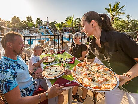 Familia comiendo pizzas en el restaurante, vista piscina, camping CAPFUN Mer et Soleil en Cap d'Agde (34).