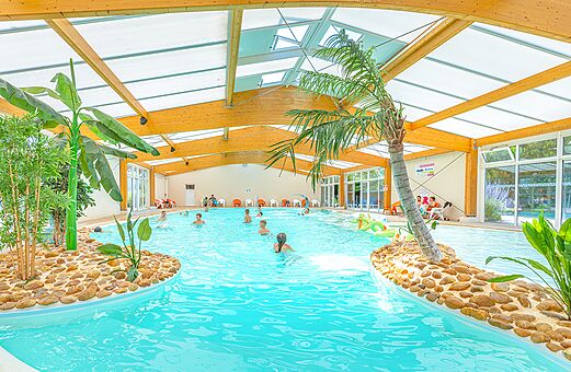 Piscina cubierta tropical con palmeras y bañistas en el camping VAGUES OCEANES Michelière, Givrand (85).