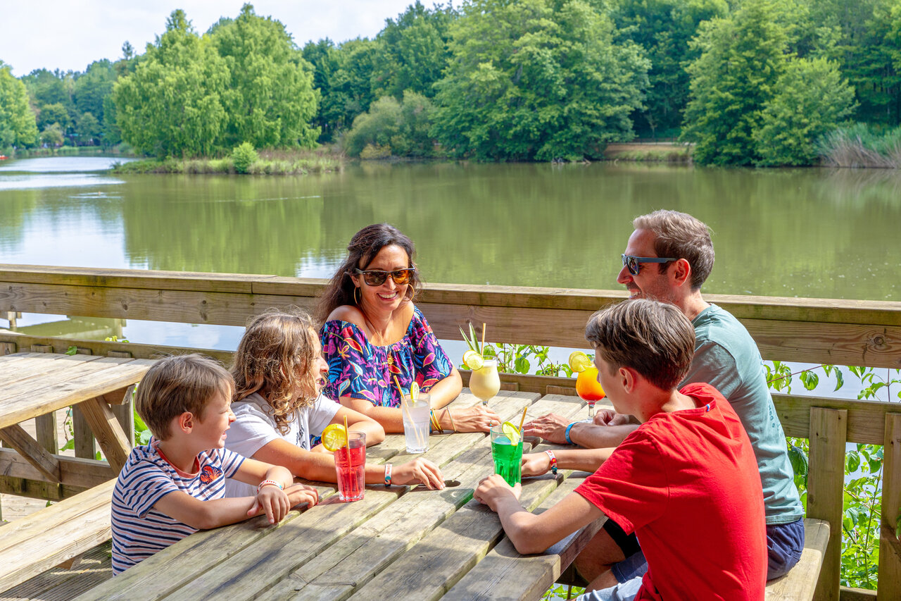 Familia sonriente bebiendo c�cteles en bar con vista lago en camping CAPFUN Moulinal en BIRON (24).