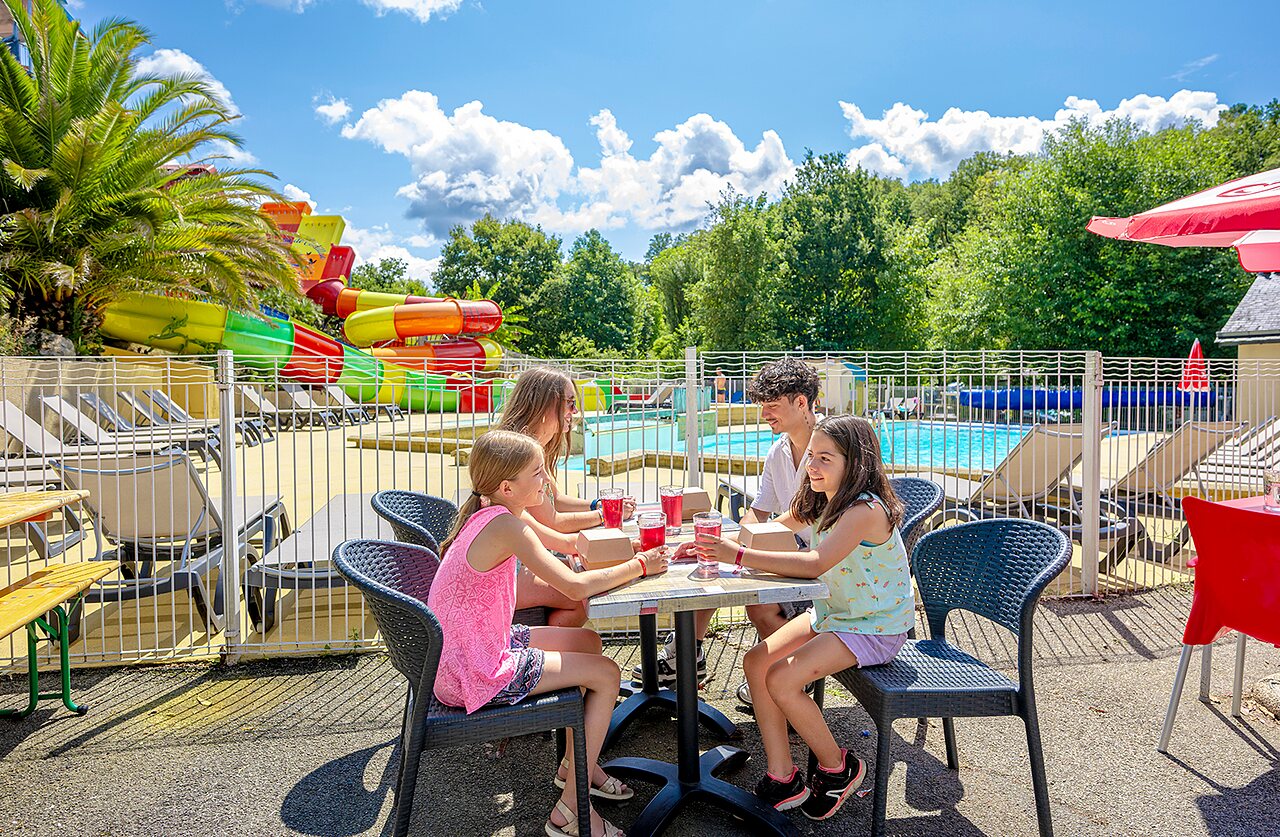 Familia disfrutando bebidas cerca de toboganes acu�ticos y piscina en camping VAGUES OCEANES Moulin de Cadillac en Noyal-Muzillac (56).