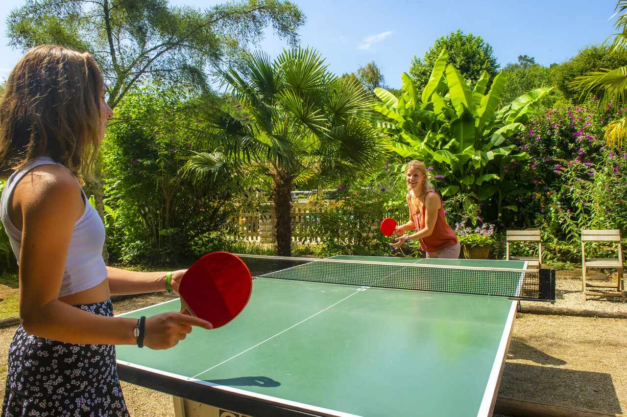 Dos mujeres jugando al tenis de mesa al aire libre en camping CLICOCHIC Moulin du Roch.
