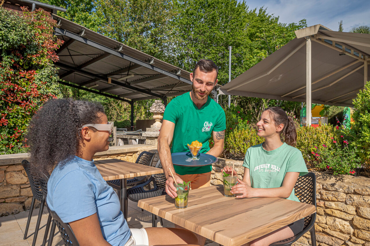 Camarero sirviendo bebidas en la terraza del camping CLICOCHIC Moulin du Roch en Saint Andre D'Allas (24).