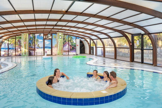 Piscina cubierta con jacuzzi y familia disfrutando en el camping VAGUES OCEANES Moustoir en Carnac (56).