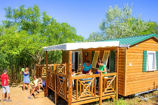 Familia en terraza de Mobil-home, jugando, en camping CAPFUN La Nina en Agde (34).