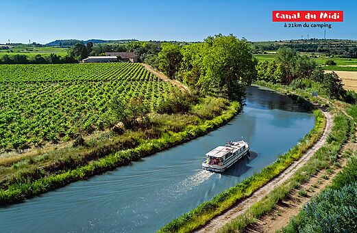 Barco navegando por el Canal du Midi, rodeado de viñedos en Occitania.