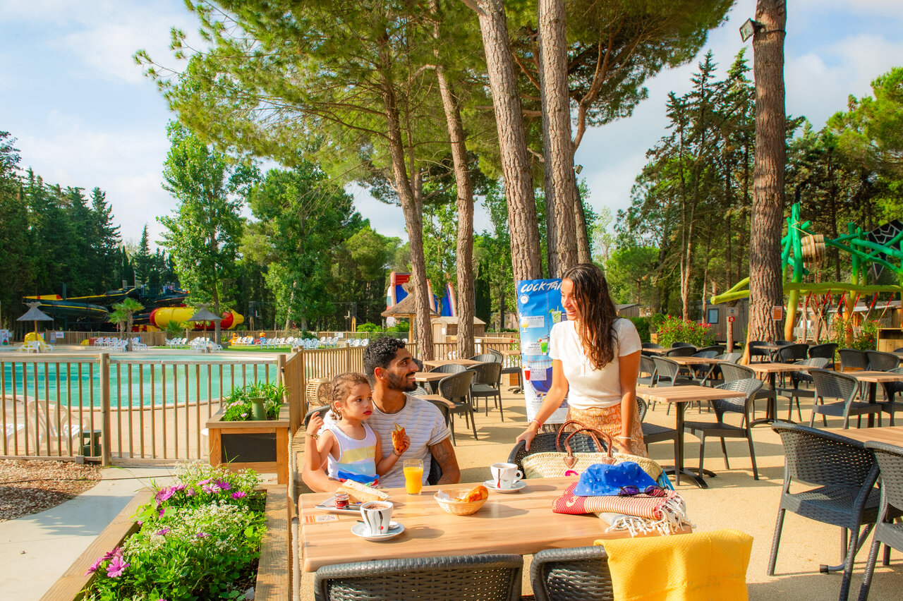 Familia desayunando en terraza junto a la piscina en el camping CAPFUN Or en La Grande Motte (34).