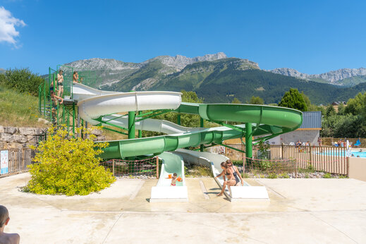 Toboganes acuáticos y niños divirtiéndose, con montañas de fondo en el camping CAPFUN Oursière en Villard de Lans (38).