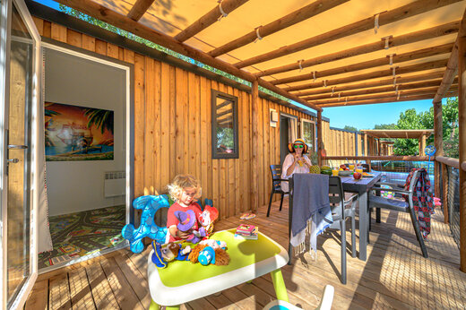 Terraza amueblada de un Mobil-home con ni�o jugando y adulto en el camping CAPFUN Pachacaid en La Mole (83).