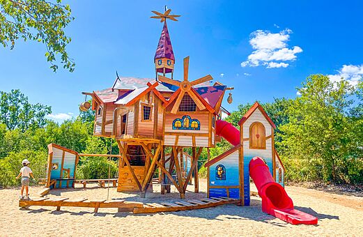 Zona de juegos de madera con tobogán rojo para niños en el camping VAGUES OCEANES Paille Basse en Souillac (46).