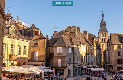Plaza histórica animada de Sarlat-la-Canéda, Dordoña, con terrazas de restaurantes.