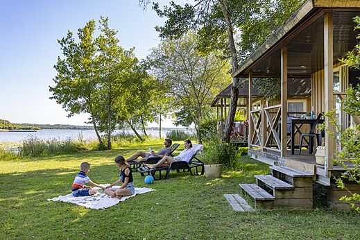 Familia frente a Mobil-home y lago, camping CAPFUN Paillotte en AZUR (40).