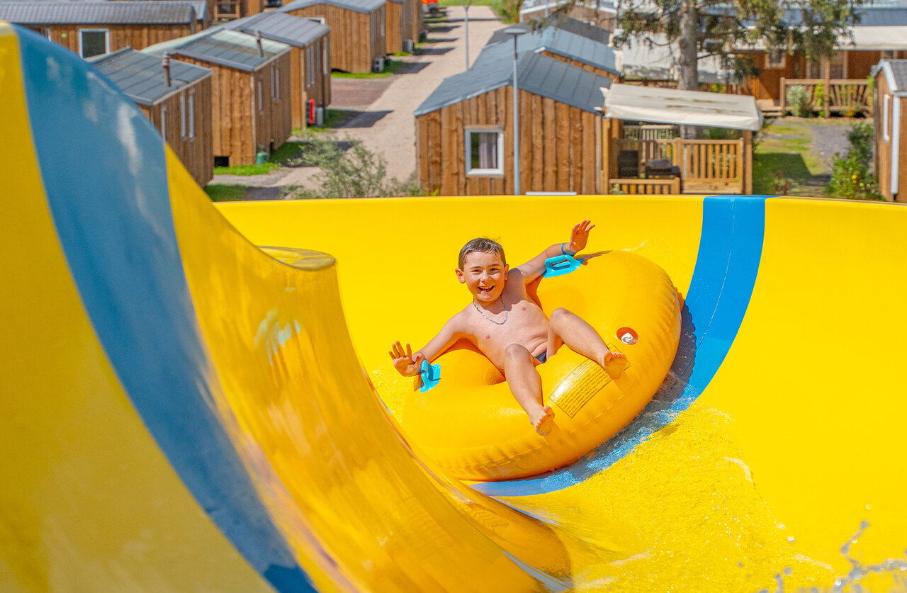 Ni�o sonriente en flotador, tobog�n acu�tico amarillo en el camping CAPFUN Palais de Gaufrette.